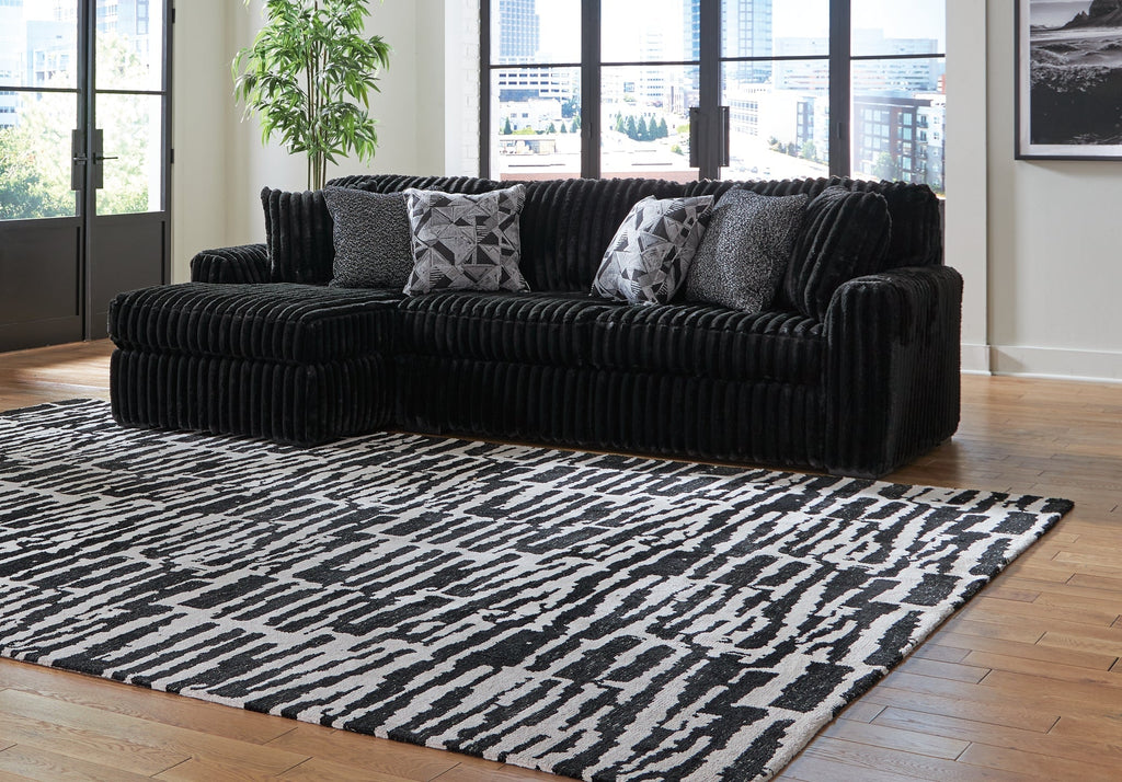 Black corduroy sofa chaise from Signature Design by Ashley® with plush cushions and modern design in a studio setting.