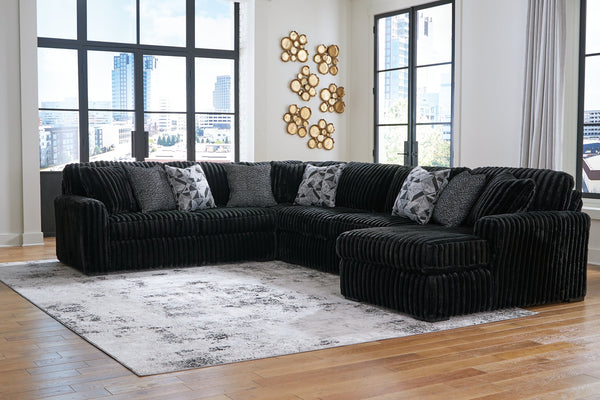 Black corduroy U-shaped sectional sofa by Ashley, featuring plush cushions and a modern design, shown in a stylish studio setting.